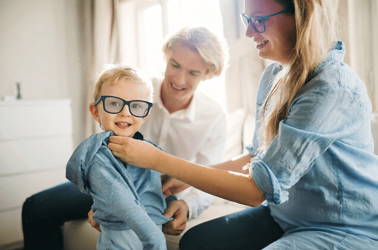 A parent helping a young boy put on his Emora glasses, which look like an ordinary pair of eyewear