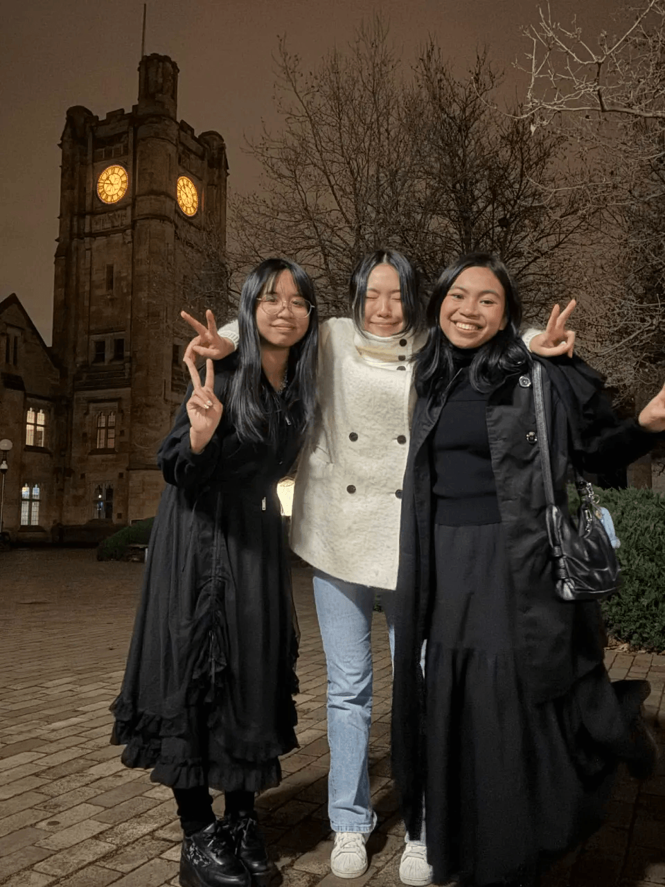 Audrey and friends posing outside a gothic clock tower at night