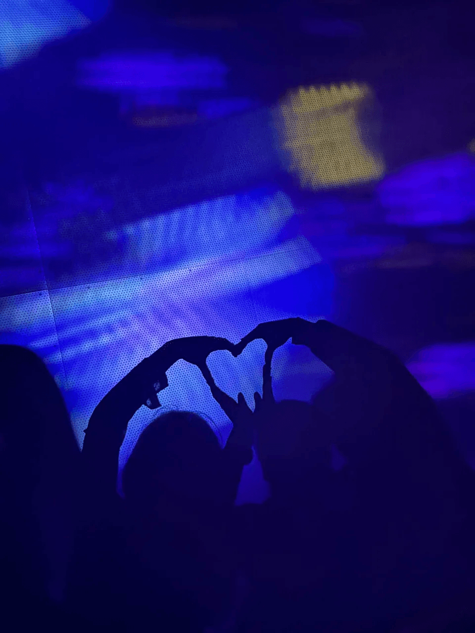 Silhouette of hands making a heart shape under blue concert lights